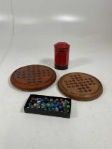 Two wooden solitaire boards together with a bag of marbles, and a tinplate Burnett Post Office money