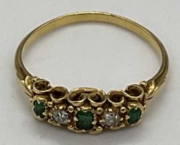 A yellow metal emerald and diamond five stone ring in elaborate scroll setting, set with three