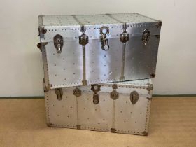 Two aluminium travelling trunks with rivet detailing, larger height 53cm, width 102cm, depth 53cm.