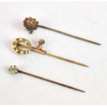 Three yellow metal stick pins contained within a velvet lined leather box, combined 3.22g.