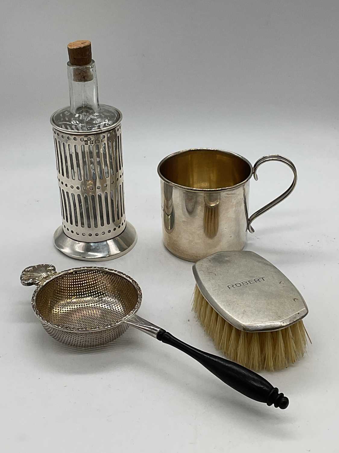 A sterling silver christening cup with engraved inscription from 1936, a silver tea strainer with