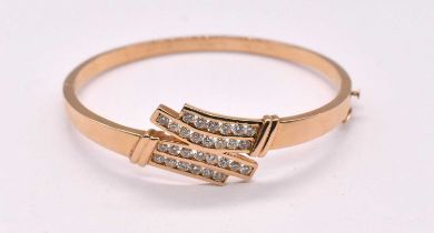 A 14ct yellow gold diamond set hinged oval bangle with four rows of channel set round brilliant