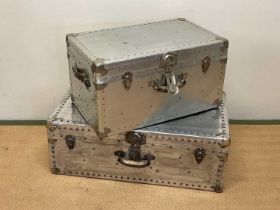 Two aluminium travelling trunks with rivet detailing, larger height 30cm, width 86cm, depth 47cm.