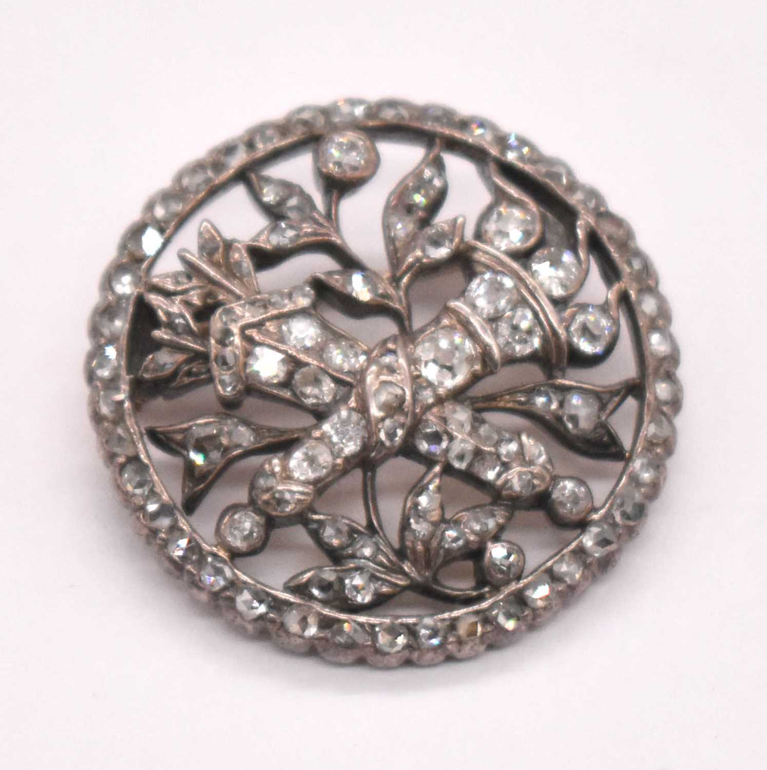 A late Victorian yellow and white metal diamond set pierced circular brooch centred with a quiver of