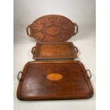 Three trays comprising a carved tray decorated with leaves, a marquetry inlaid tray with brass
