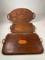 Three trays comprising a carved tray decorated with leaves, a marquetry inlaid tray with brass