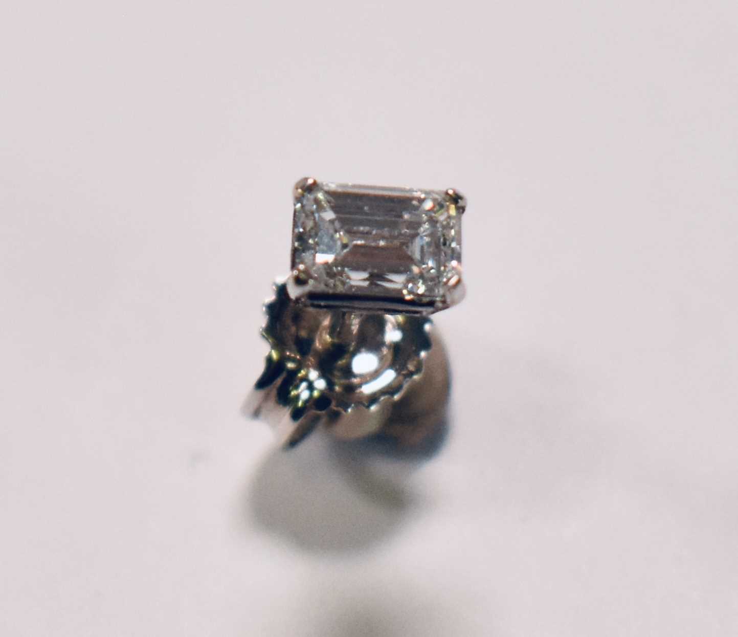 A white metal single diamond ear stud, the emerald cut stone weighing approx 0.33ct, corner claw set