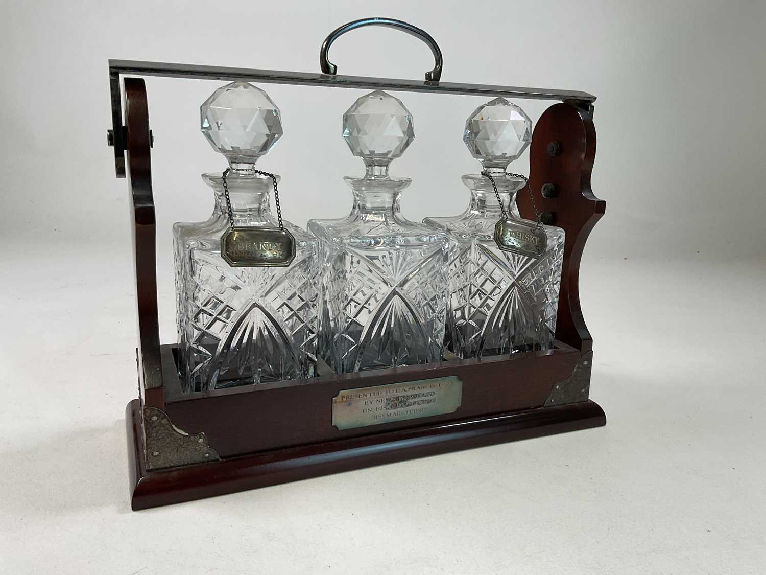 A three bottled tantalus, with two hallmarked silver spirit labels titled 'Brandy' and 'Whisky',