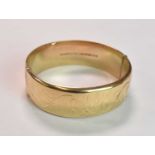 A 9ct yellow gold oval engraved hinged bangle, internal width 57mm, approx 23.2g.