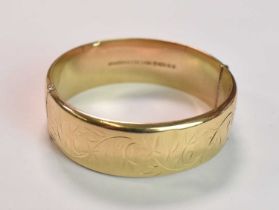 A 9ct yellow gold oval engraved hinged bangle, internal width 57mm, approx 23.2g.
