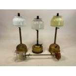Three Tilley lamps, one with yellow shade, the others with white glass shades and a wall mounted