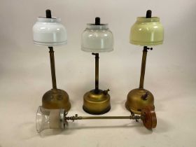 Three Tilley lamps, one with yellow shade, the others with white glass shades and a wall mounted