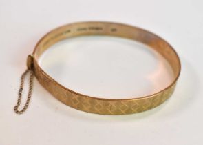 A 9ct yellow gold engraved oval hinged bangle, internal width 60mm, approx 14.7g.