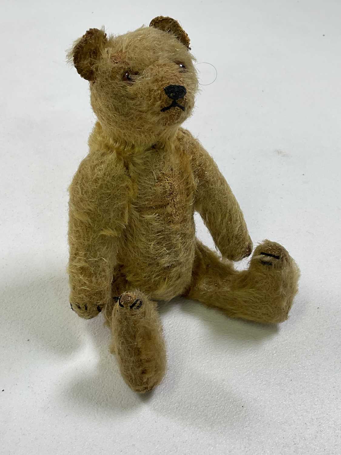 A small vintage mohair Teddy bear with glass eyes and a hump back, stitched nose, paws and feet,