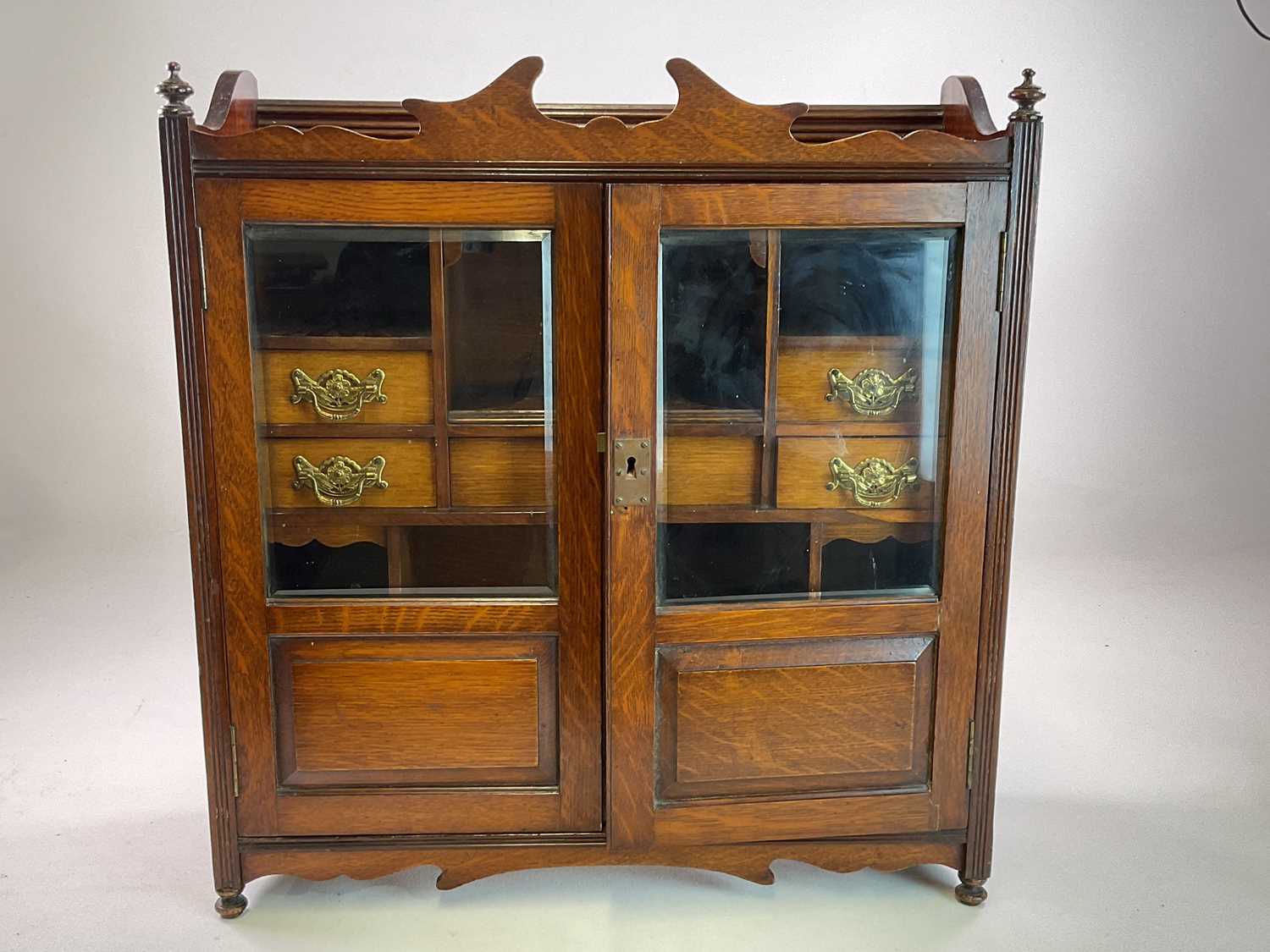 A Victorian oak smoker's cabinet with double glass doors and seven drawers and shelves to