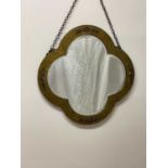 An Arts and Crafts mirror of quatrefoil form with bevelled glass and hammered brass frame