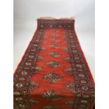 A Bokhara hand knotted runner with repeating design on a terracotta ground, 265 x 80cm