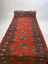 A Bokhara hand knotted runner with repeating design on a terracotta ground, 265 x 80cm