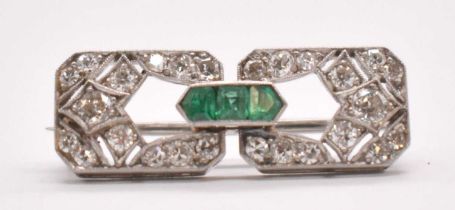 An Art Deco white metal emerald and diamond brooch set with three emeralds to the central raised