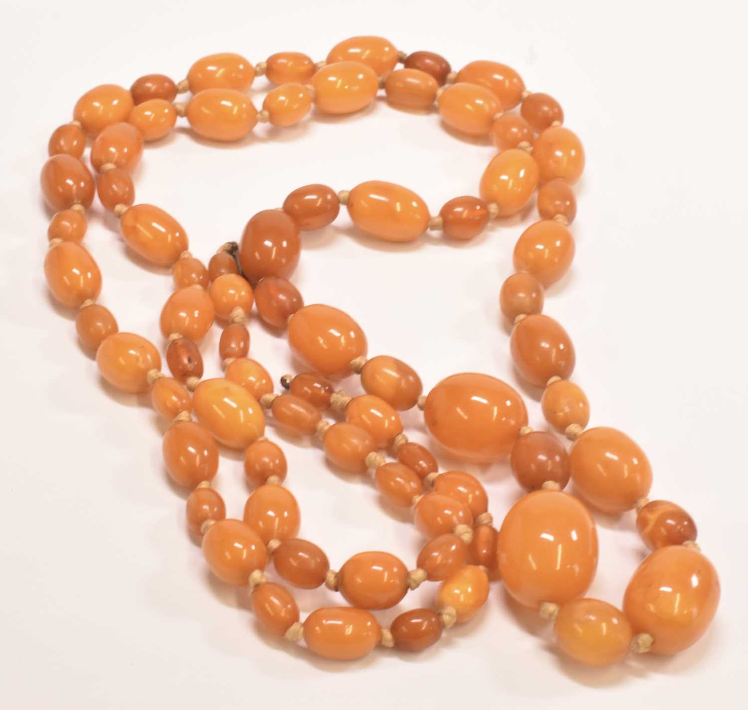 A vintage hand tied graduated butterscotch/egg yolk amber bead necklace, length 114cm, largest