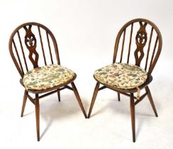 ERCOL; a pair of dark elm stick back open armchairs upholstered with cream cushions, on tapering
