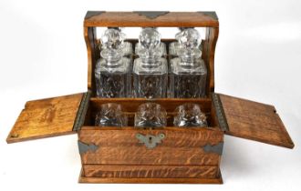 An early 20th century brass bound oak tantalus with three pressed glass square decanters enclosed to