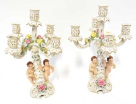 DRESDEN; a pair of 20th century figural four-branch candlesticks, each with putti and encrusted with