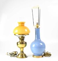 A reproduction oil lamp with mustard-coloured shade, together with a similar example with painted