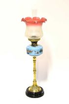 A Victorian brass oil lamp with painted blue glass well and a matched etched cranberry and opaque