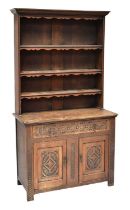 An early 20th century carved oak dresser with enclosed plate rack of three shelves, above a base