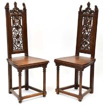 A pair of carved oak hall chairs with pierced floral back panels, arched tops terminating in