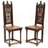 A pair of carved oak hall chairs with pierced floral back panels, arched tops terminating in