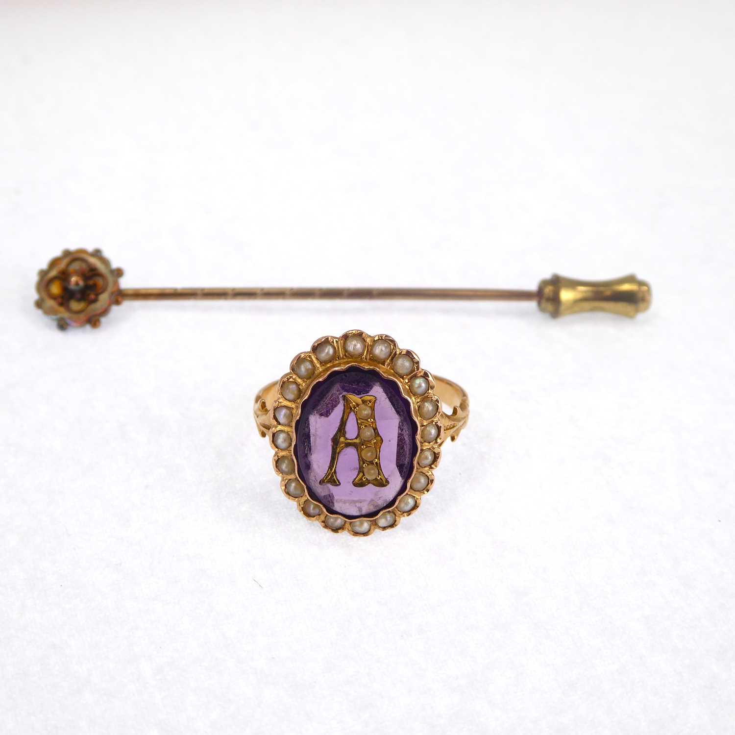 A Victorian gold ring with central initial A, with an amethyst bezel set stone within a border of