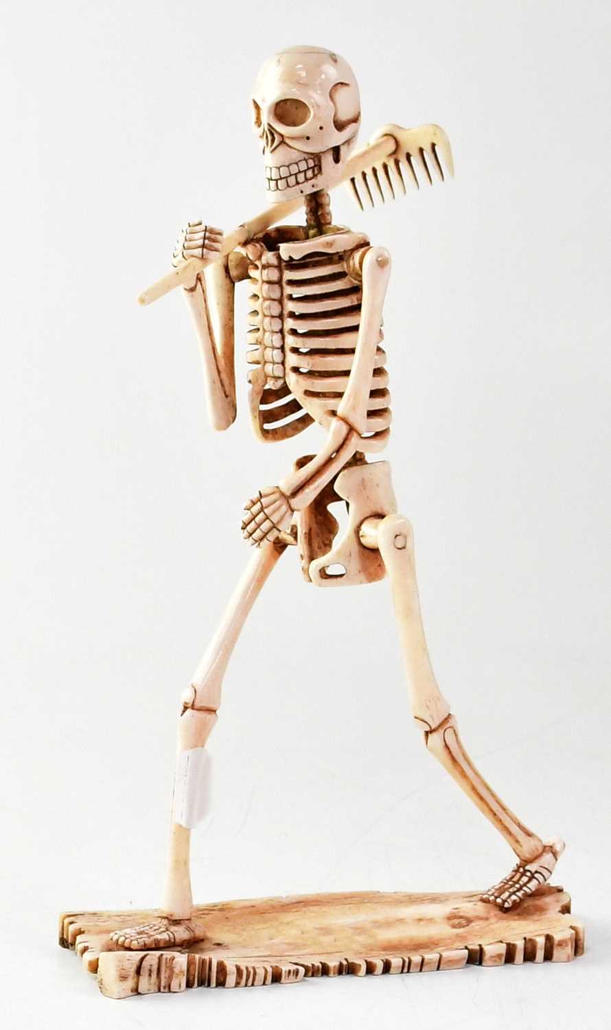 A large carved bone model of a skeleton carrying a rake, height 29cm.