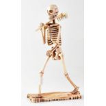 A large carved bone model of a skeleton carrying a rake, height 29cm.