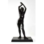 A bronzed figure of a nude female with her arms raised above her head, on a square section base,