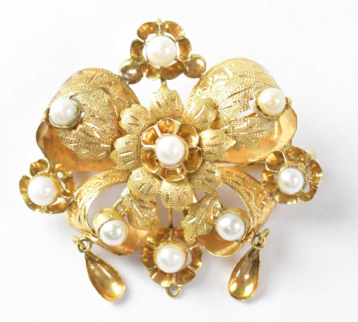 A yellow metal brooch in the form of a flower head surrounded by leaves, set with nine seed