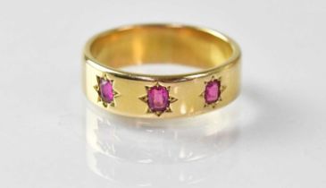 An 18ct gold wide band ring, star set with three small rubies, size N, approx. 5.7g. Condition