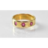 An 18ct gold wide band ring, star set with three small rubies, size N, approx. 5.7g. Condition