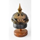 A WWI Prussian M1915 pickelhaube on stand (af). Condition Report: Leather cracking throughout, brass