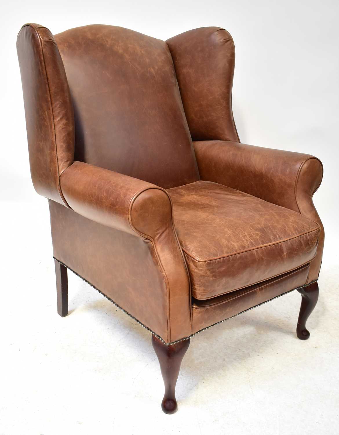 A modern brown leather wing armchair with studs, on mahogany cabriole feet, height 105cm.