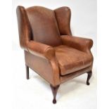 A modern brown leather wing armchair with studs, on mahogany cabriole feet, height 105cm.