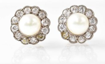 A pair of stud earrings set with pearls in a white stone surround, the butterfly backs stamped '