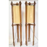 A pair of oak Arts and Crafts style standard lamps, each with three carved supports and cream drapes