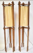 A pair of oak Arts and Crafts style standard lamps, each with three carved supports and cream drapes