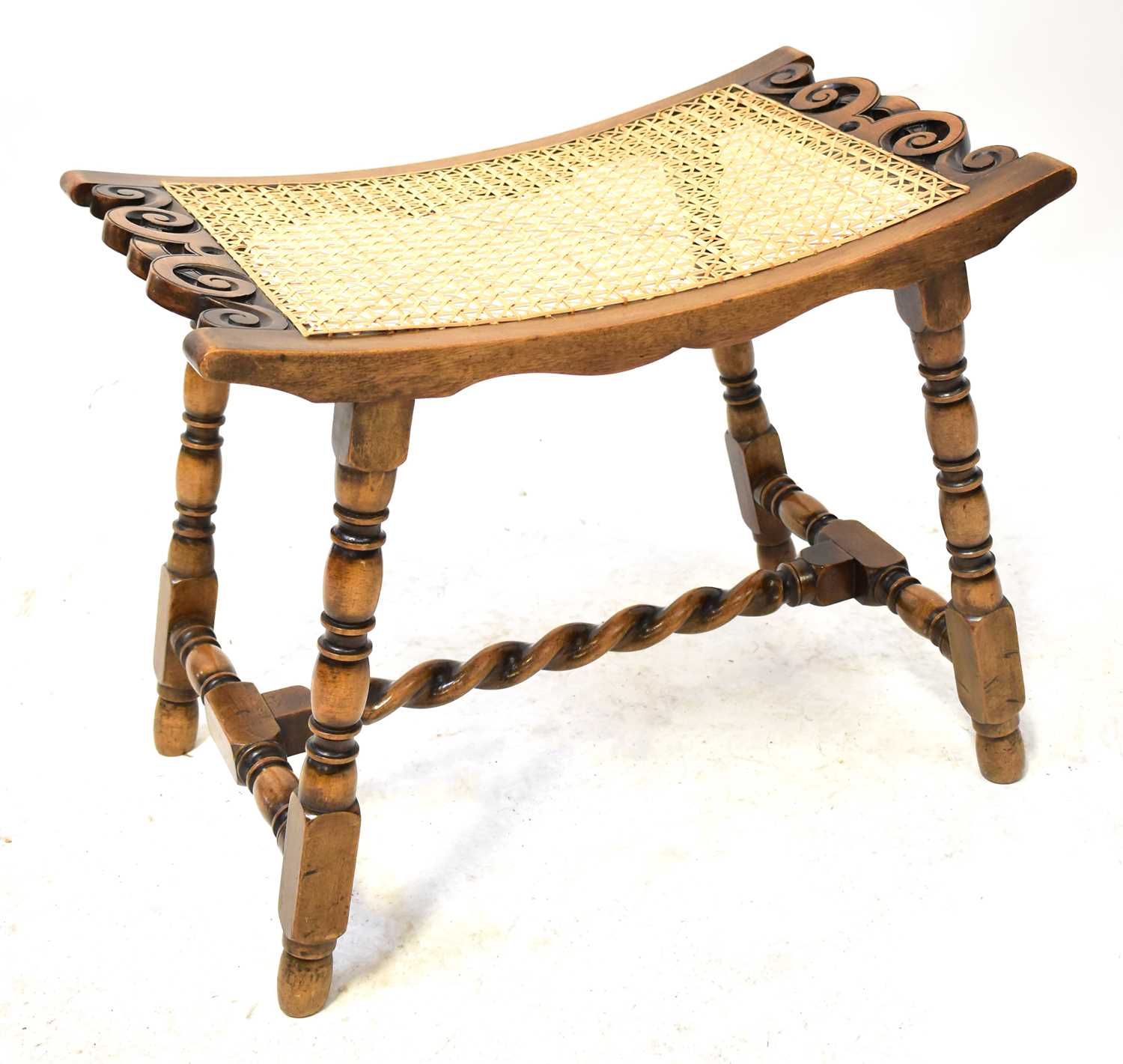 An early 20th century cane-topped stool of curved form, with turned square supports united by