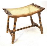 An early 20th century cane-topped stool of curved form, with turned square supports united by