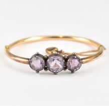 An Edwardian gold hinged bracelet with three bezel set cut amethyst stones, with safety chain, hinge