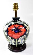 MOORCROFT; a lamp decorated with poppies on a blue, cream and green ground, on a circular wooden