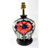MOORCROFT; a lamp decorated with poppies on a blue, cream and green ground, on a circular wooden
